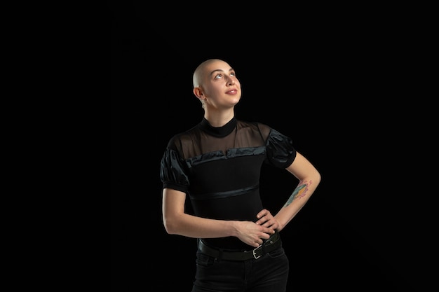 Monochrome portrait of young bald woman on black wall