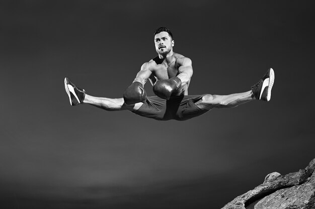 Монохромный снимок красивого подходящего молодого мужского гимнаста, прыгающего высоко, делающего шпагаты в воздухе, спортивного фитнеса, образа жизни Copyspace, гибкого растяжения ног, энергичной деятельности, гимнастики, прыжка, мухи, концепции.