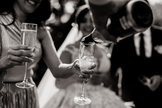 Monochrome view of a  pouring bottle into glasses and champagne glasses in tender women's hands