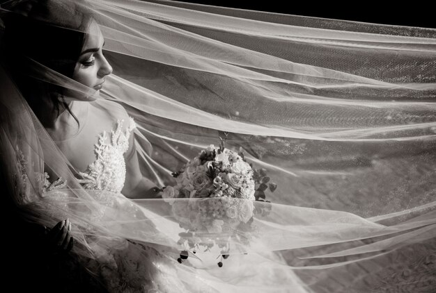 Monochrome view of a tender beautiful bride with wedding bouquet and long veil with closed eyes