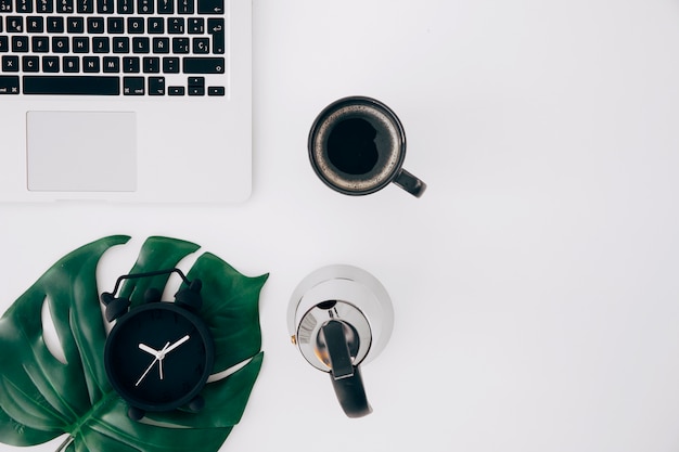 Monster leaf on alarm clock; kettle; coffee cup and laptop on white background