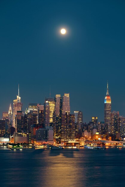 밤에 도시 스카이라인이 있는 맨해튼 미드타운 위로 달이 뜨다