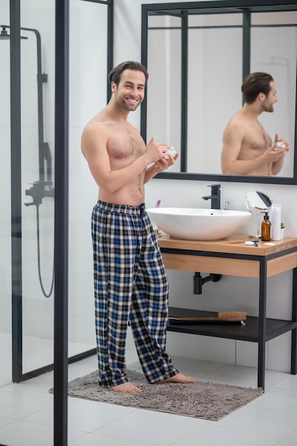 Free photo morning routine. man in plaid home pants standing at the mirror