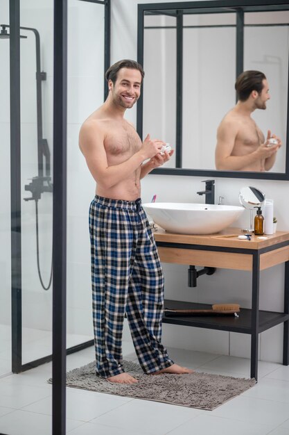 Morning routine. Man in plaid home pants standing at the mirror