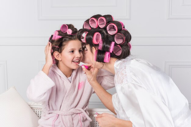 Mother applying bright lip gloss on daughters lips