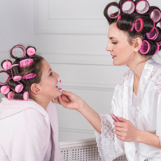 Mother applying lip gloss on daughters lips