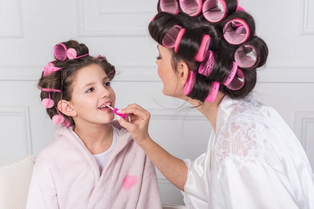 Mother applying pink lip gloss on daughters lips