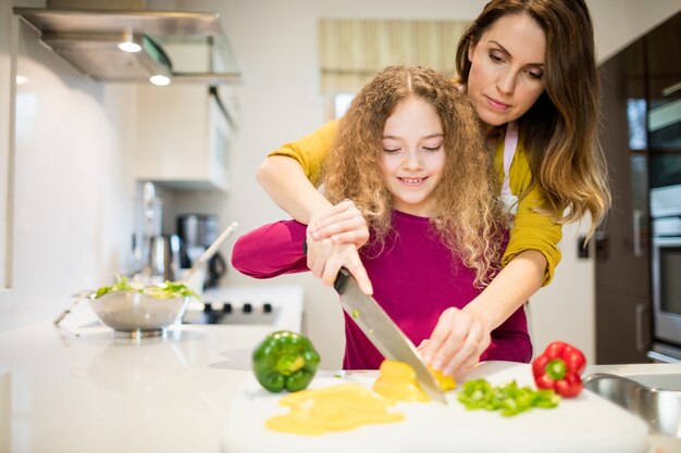 Мать помогая дочь в резки овощей на кухне