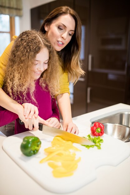 Mother assisting daughter in cutting vegetables in kitchen