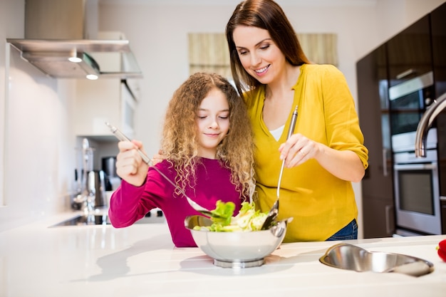 Mother assisting daughter in making salad