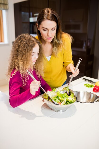 Mother assisting daughter in making salad