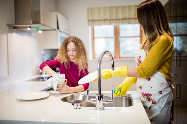 Free photo mother assisting daughter in washing plate in kitchen