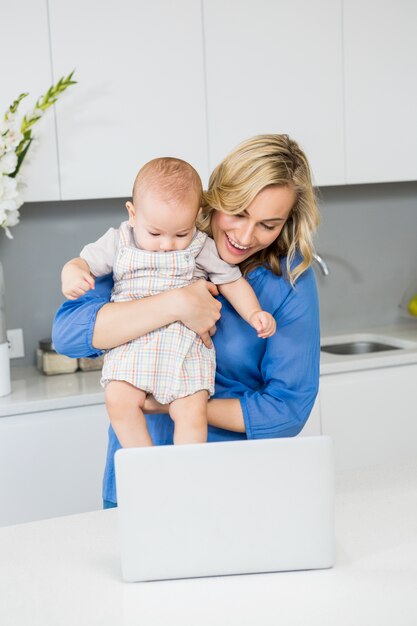 Mother and baby boy using laptop in kitchen