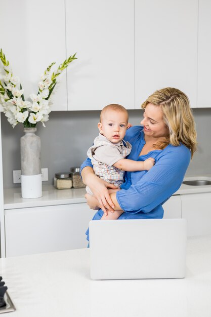 Mother and baby boy using laptop in kitchen