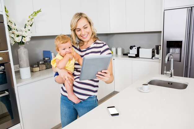 Mother and baby girl using digital tablet in kitchen