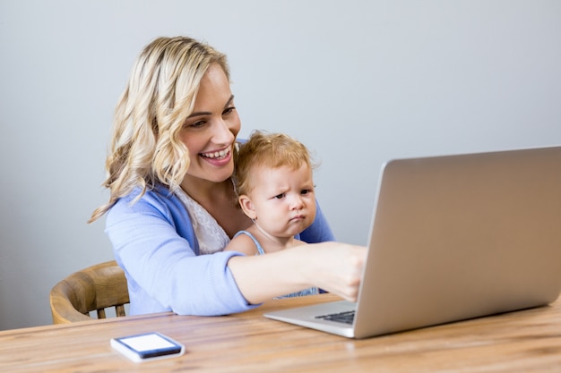 Mother and baby sitting at table and using laptop