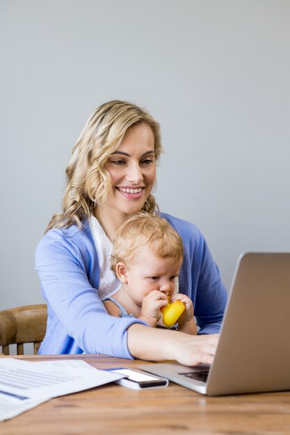 Mother and baby sitting at table and using laptop