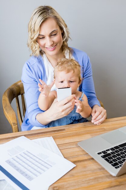 Мать и ребенок сидит за столом и с помощью мобильного телефона
