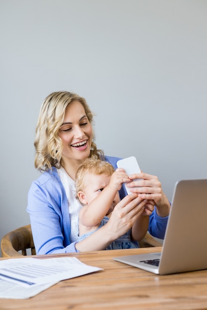 Mother and baby sitting at table and using mobile phone