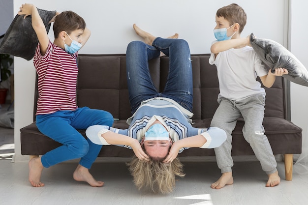 Мать раздражена дома детьми, которые играют с подушками, имея медицинские маски на