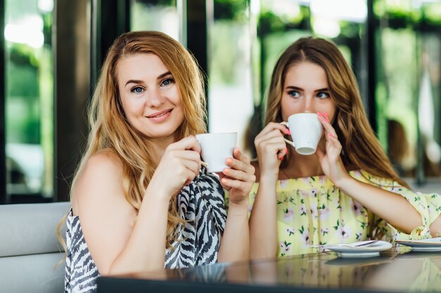 Mother and blonde daughter talk and smile while drink latte