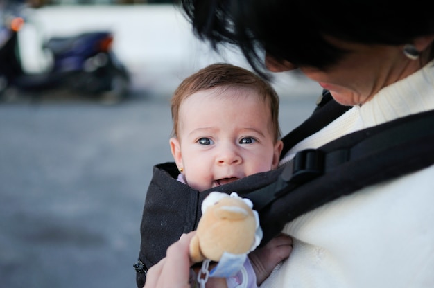 Mother carrying her baby girl in a baby carrier outdoors