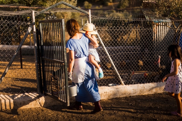 Mother carrying her daughter entering in the poultry gate