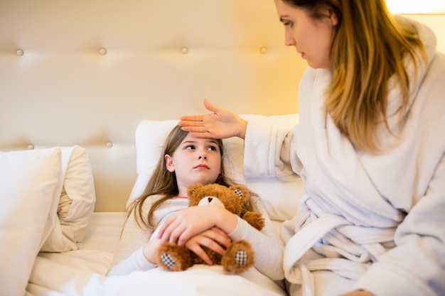 Mother checking fever of her daughter in bedroom