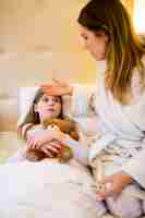 Free photo mother checking fever of her daughter in bedroom