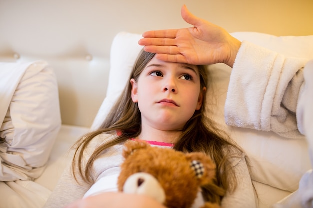 Mother checking fever of her daughter in bedroom