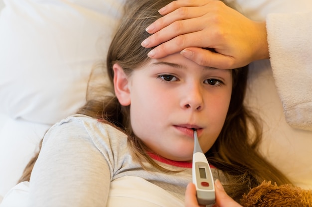 Mother checking fever of her daughter in bedroom