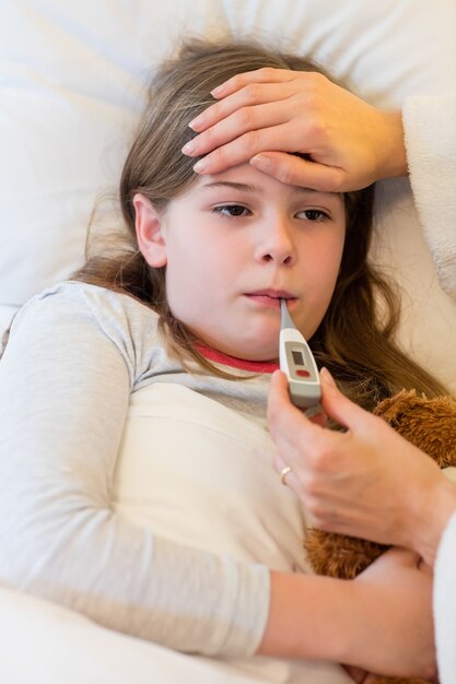 Mother checking fever of her daughter in bedroom