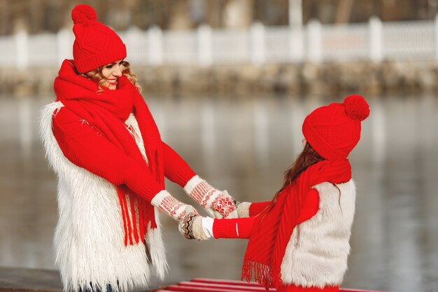 家族のクリスマス休暇にニットの冬の帽子をかぶった母と子。ママと子供のための手作りのウールの帽子とスカーフ。子供のための編み物。ニットアウター。公園の女性と少女。