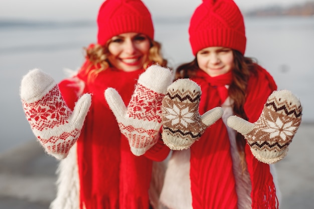 家族のクリスマス休暇にニットの冬の帽子をかぶった母と子。ママと子供のための手作りのウールの帽子とスカーフ。子供のための編み物。ニットアウター。公園の女性と少女。