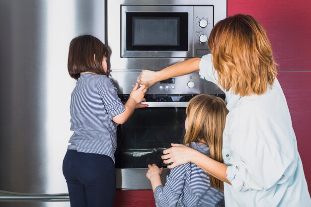 Mother and children closing oven in kitchen