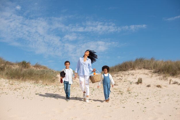 화창한 날에 해변을 걷고 있는 엄마와 아이들. 야외에서 함께 시간을 보내는 아프리카계 미국인 가족. 여가, 가족 시간, 육아 개념