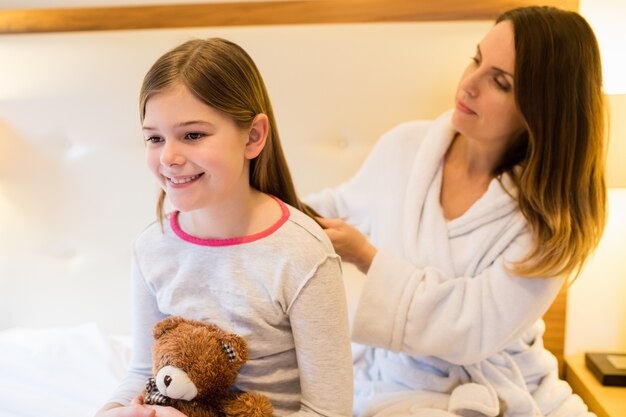 Mother combing her daughters hair in bedroom