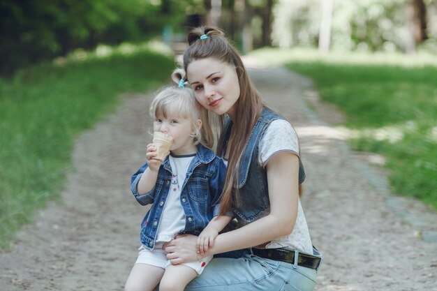 Mother crouching holding a hand to her daughter while eating an ice cream