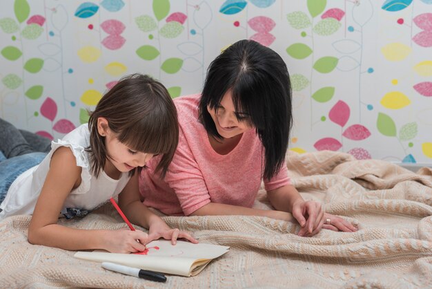 Mother and cute daughter drawing lying on bed