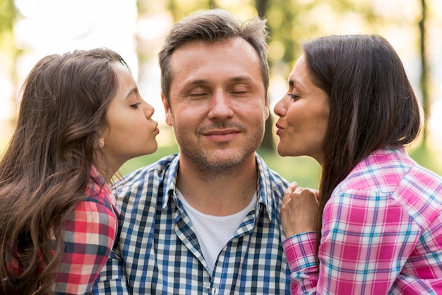 Madre e figlia carina che bacia padre nel parco