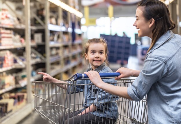 장바구니를 사용하여 슈퍼마켓에서 쇼핑하는 파란색 셔츠에 엄마와 딸