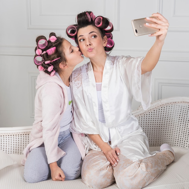 Mother and daughter in curlers taking selfie on couch