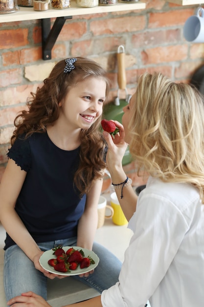 Mother and daughter eating strawberries in the kitchen