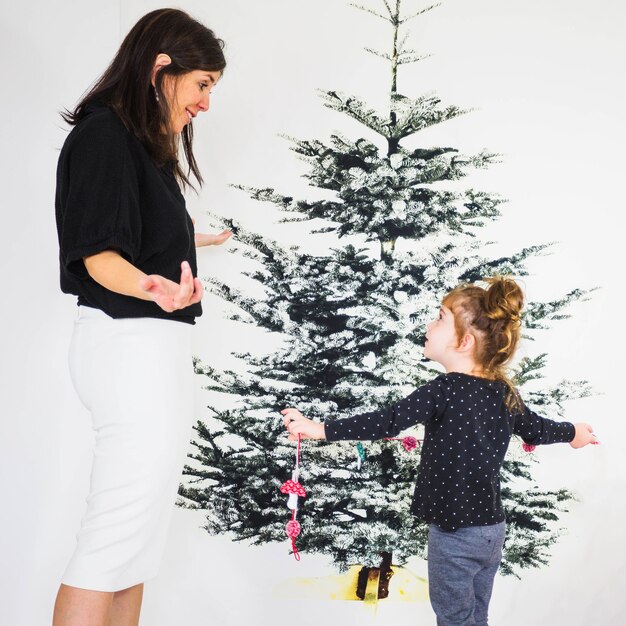 Free photo mother and daughter in front of christmas tree