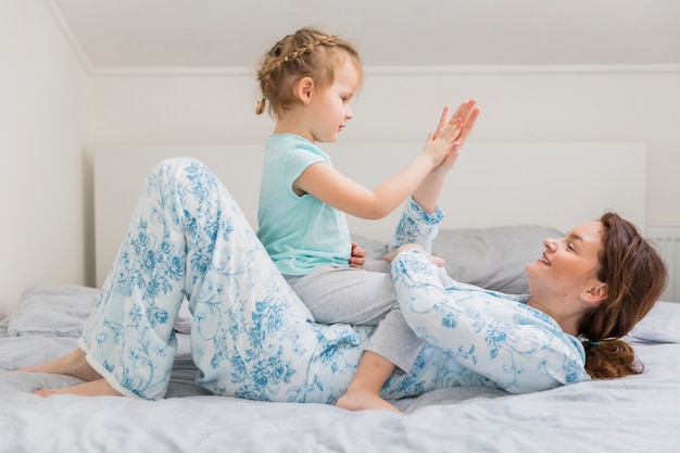 Mother and daughter giving high five while lying on bed in home