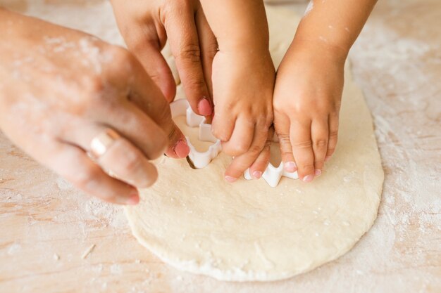 Руки матери и дочери режут тесто для печенья