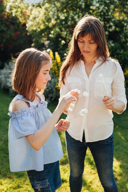 Free photo mother and daughter holding marshmallow skewer in garden