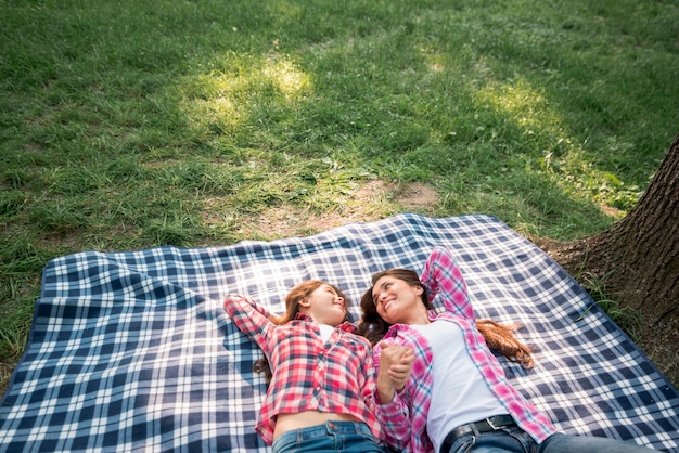 어머니와 딸이 공원에서 담요에 누워 그들의 손을 잡고