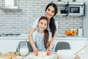 Free photo mother and daughter holding tray with unbaked cookies together in kitchen