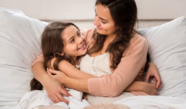 Mother and daughter hugging each other in bed
